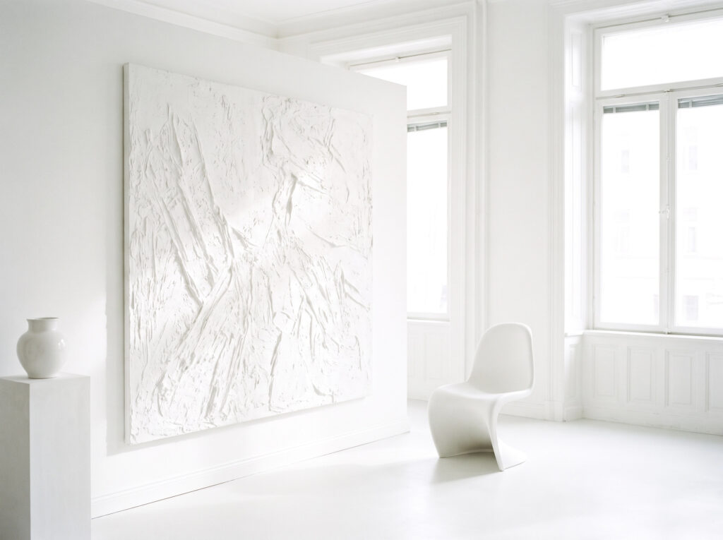 The purity of white in Minimalist Color Psychology: A bright white-on-white interior with a textured painting.